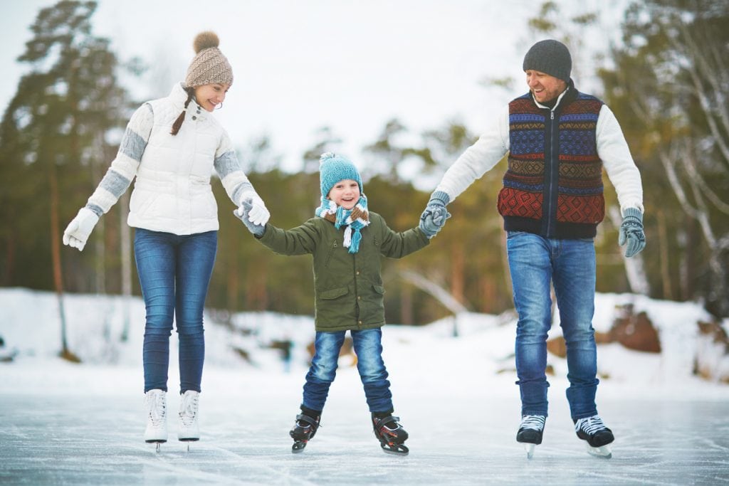 Cute boy and his parents skating together on the rink
